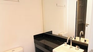 A modern bathroom with a white toilet, black countertop, white sink, and a large mirror. - Vn Consolação 710 (São Paulo)