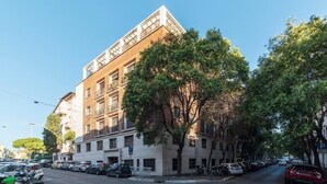 A multi-story building with a corner entrance, parked cars, and trees along the street. - HospitalityRome Artists House (Roma)