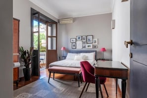 Ein Schlafzimmer mit Bett, Nachttischen, Schreibtisch, Stuhl, einem Blumentopf und einem Fenster.