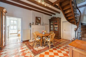 A dining area with a wooden table and chairs, a patterned rug, a wooden cabinet, and a staircase.