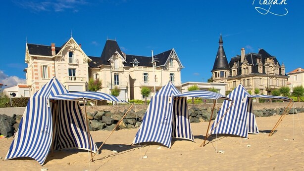 A beach with striped beach umbrellas and a large historic building in the background. - Charming Family Home from 1880 in the Heart of Charente-Maritime (Boutenac Touvent)