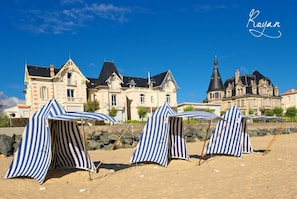 A beach with striped beach umbrellas and a large historic building in the background.