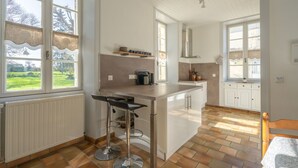 A kitchen with a central island, bar stools, a radiator, and large windows. - Charming Family Home from 1880 in the Heart of Charente-Maritime (Boutenac Touvent)