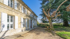 A stone building with multiple windows and doors, a dirt pathway, and a large tree. - Charming Family Home from 1880 in the Heart of Charente-Maritime (Boutenac Touvent)