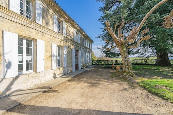 A stone building with multiple windows and doors, a dirt pathway, and a large tree.