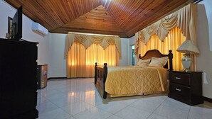 Ein Schlafzimmer mit Holzbalkendecke, einem Bett mit Kopfteil, Vorhängen, einem Nachttisch und einer Kommode.