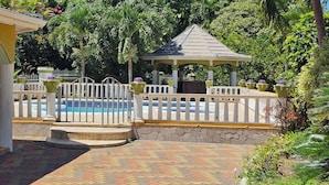 Ein Poolbereich mit Pavillon, umgeben von einem weißen Zaun und üppiger Bepflanzung.