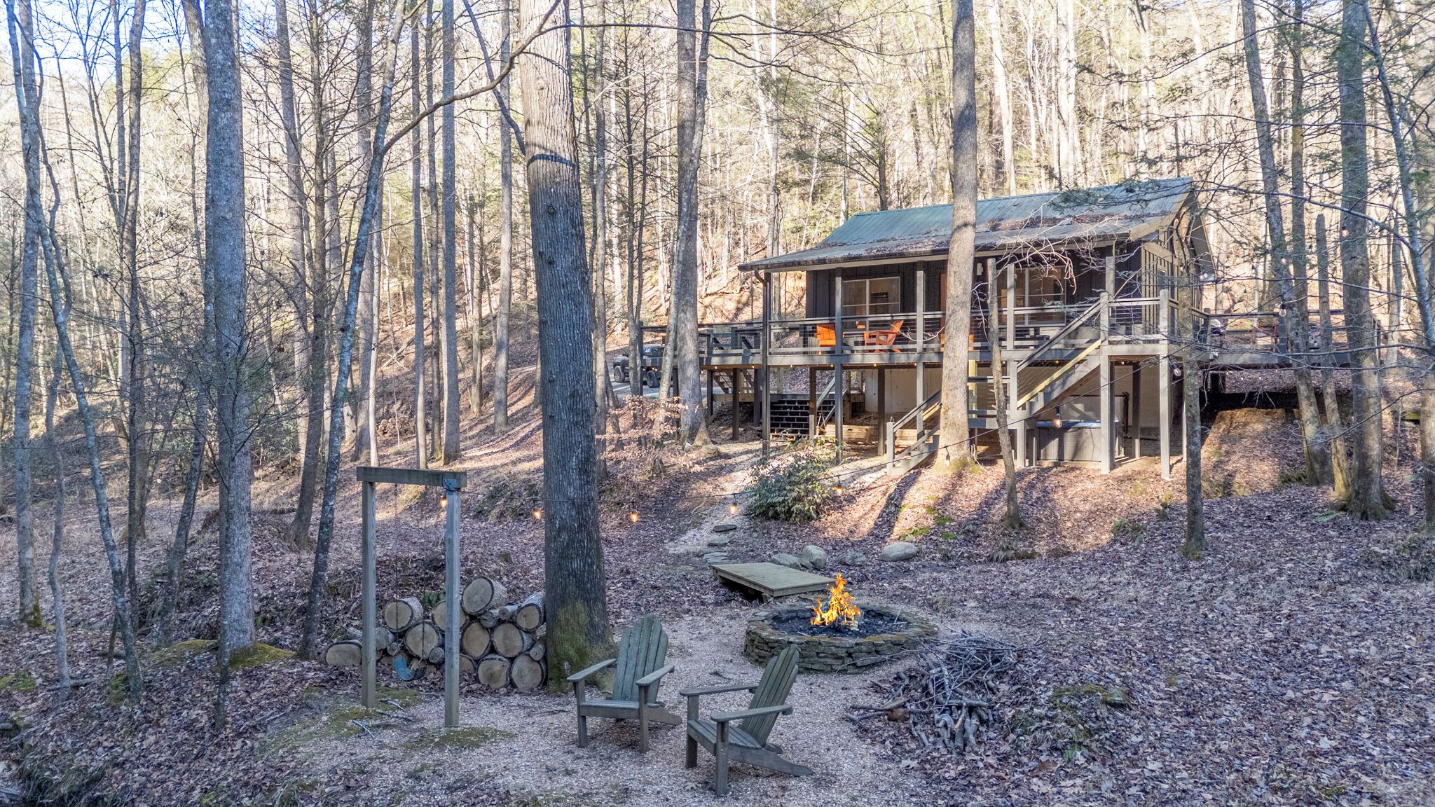 Une cabane dans une forêt, dotée d’une terrasse, d’un foyer et de meubles pour se détendre en plein air.