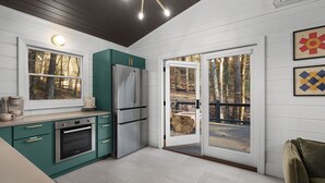 A modern kitchen with a built-in oven, stainless steel refrigerator, and a large window overlooking a forested area. - 706 On The Creek - Mid-century modern-inspired vibe - Blue Ridge, GA (Blue Ridge)