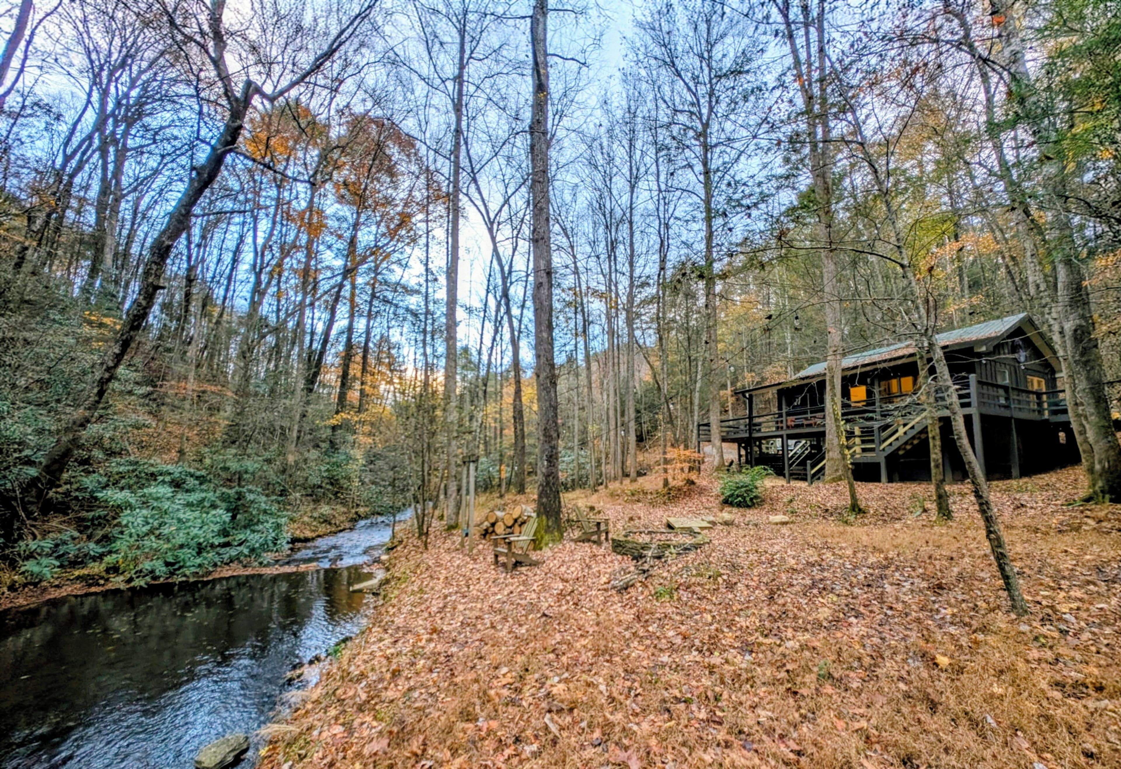 A cabin with a deck and a river in a forest.