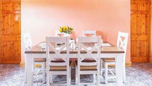 Un coin repas avec une table en bois et des chaises blanches, un vase de fleurs jaunes et un tableau encadré au mur.
