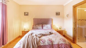 Une chambre à coucher avec un grand lit, deux tables de chevet avec des lampes, une porte en bois et une cabine de douche en verre.