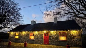 Une petite maison en pierre avec une porte rouge, de nombreuses fenêtres et des guirlandes lumineuses.