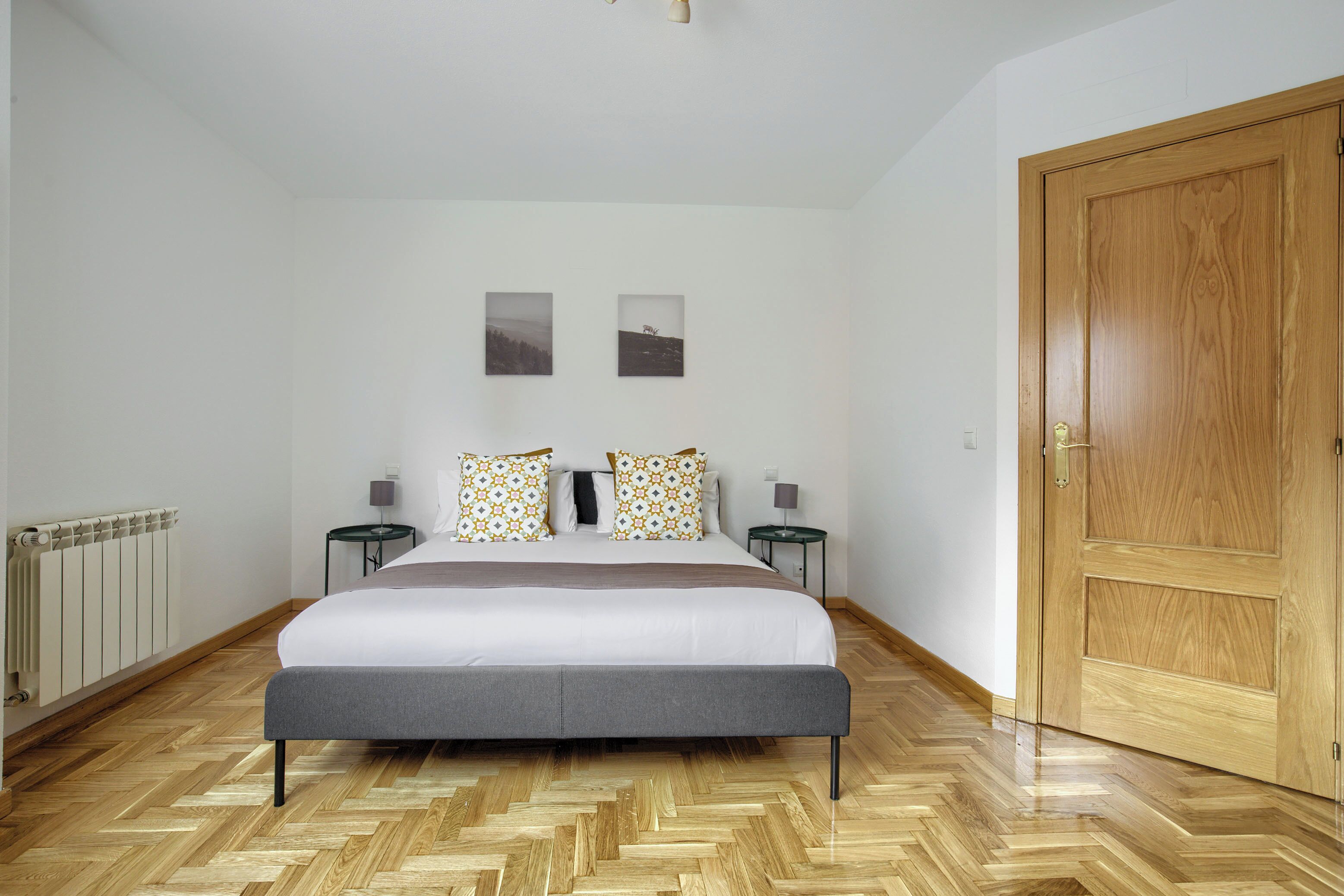 A bedroom with a bed, two nightstands, a wooden door, and a radiator.