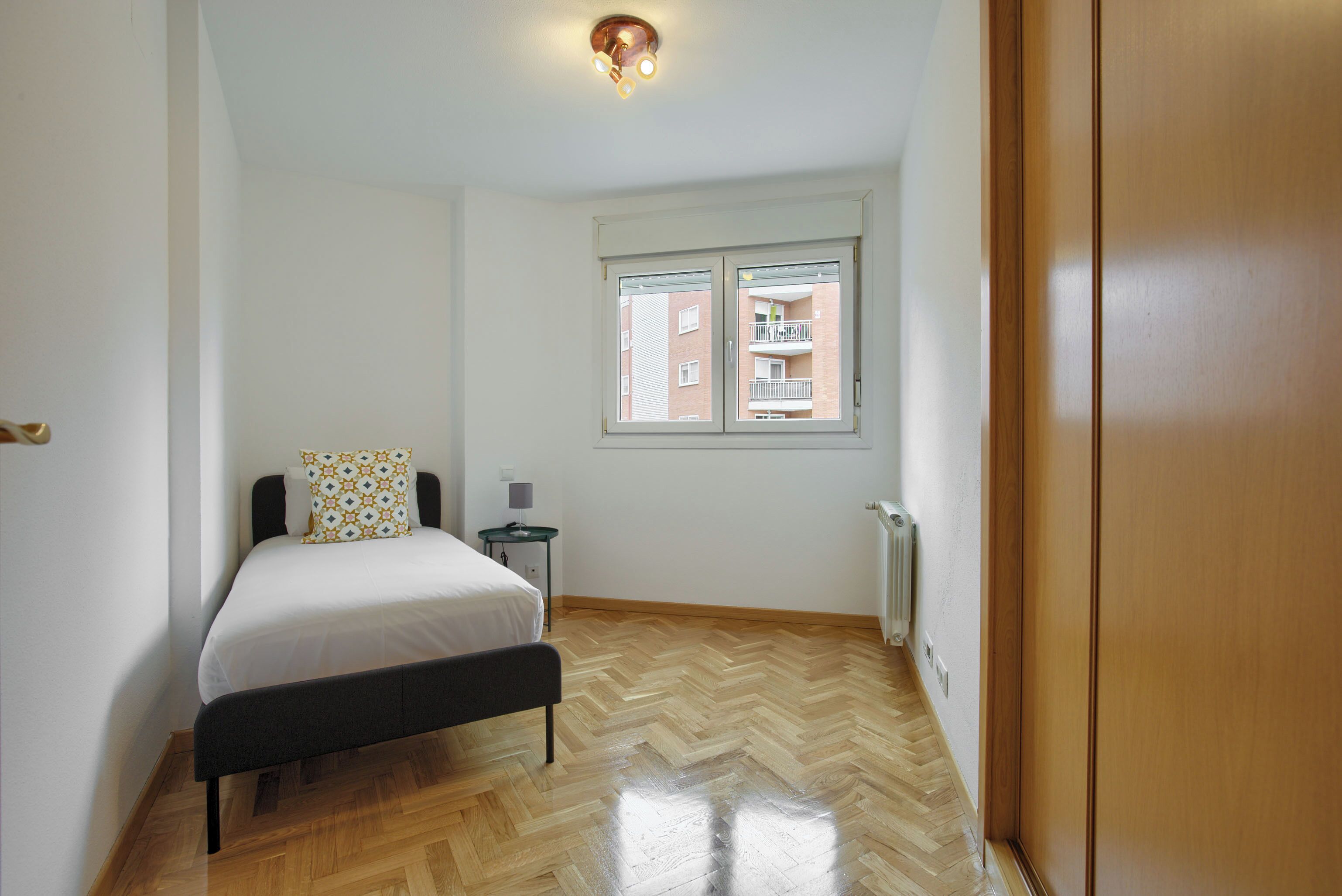 Un dormitorio con cama, mesita de noche, ventana y radiador.