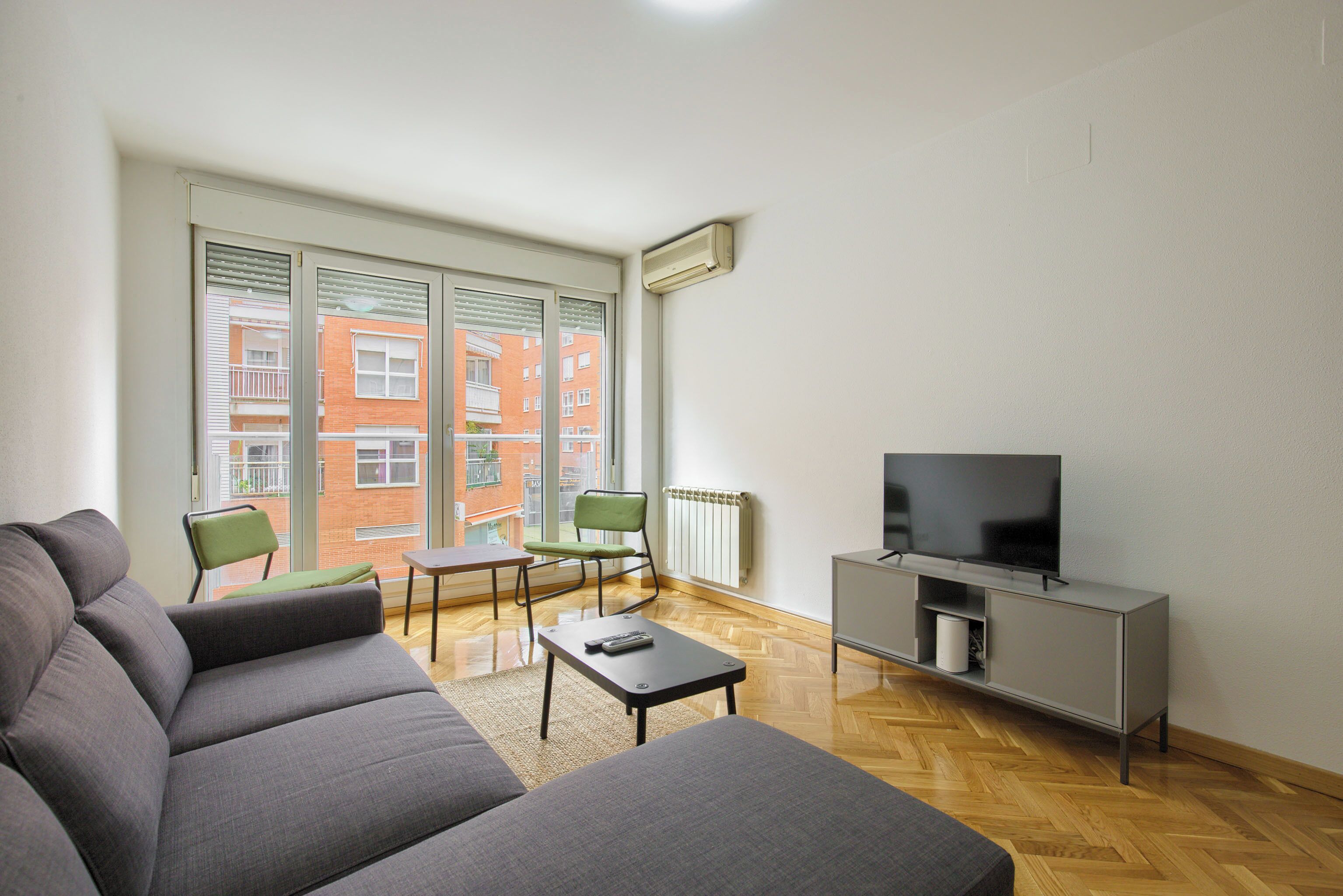 A modern living room with a grey sofa, a small table, a green chair, and a TV on a grey cabinet.