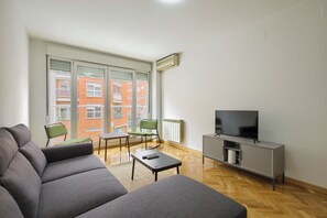 Un soggiorno moderno con un divano grigio, un tavolino, una poltrona verde e una TV su un mobile grigio.