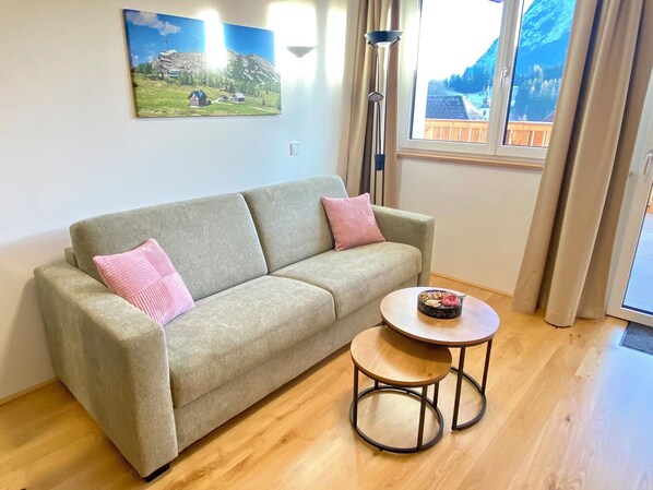 Un salon avec un canapé, deux coussins, une petite table ronde et un tableau accroché au mur.