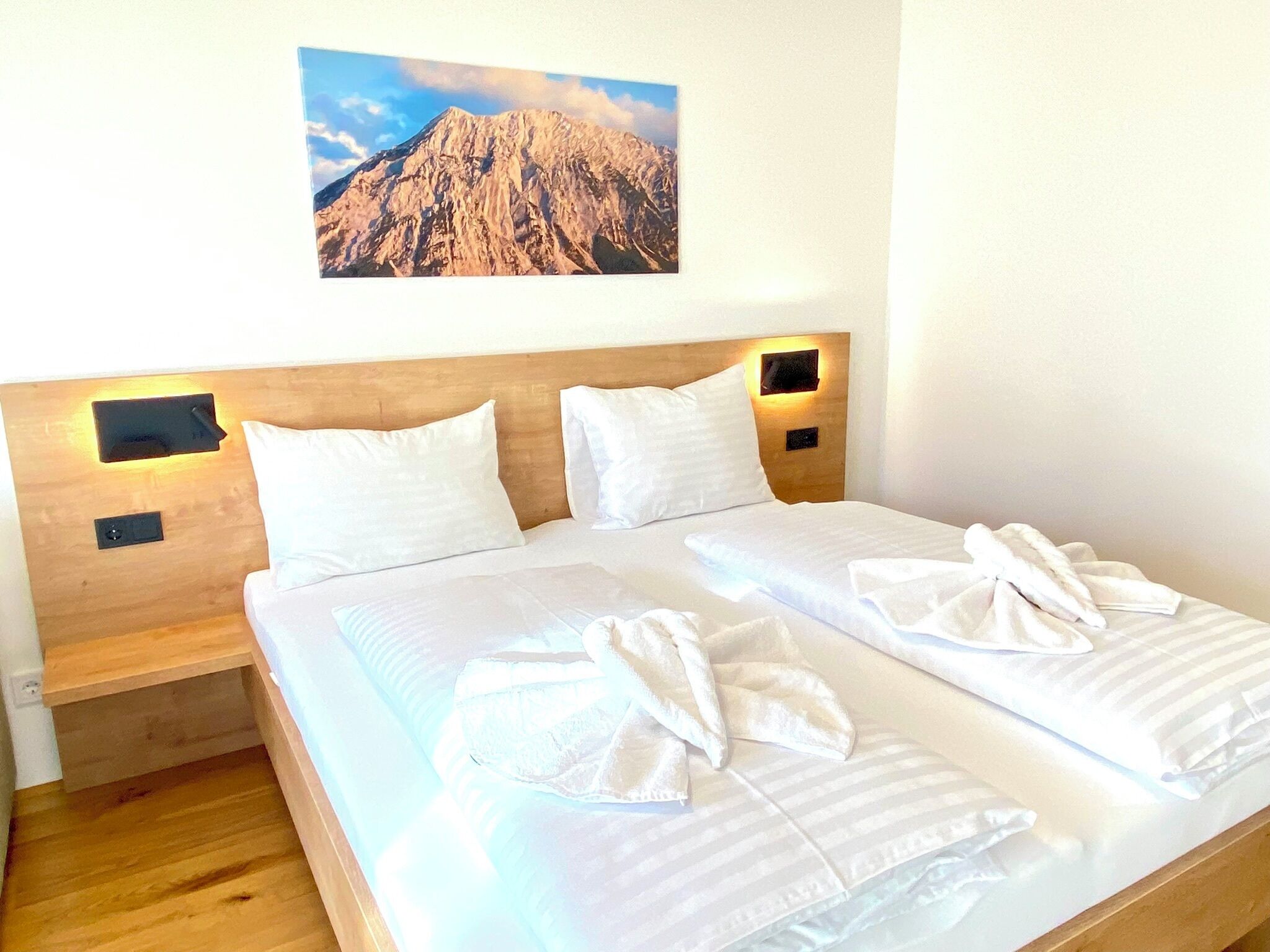 Ein Doppelbett mit weißen Bettwäsche, zwei Kissen und zwei Handtücher, die ordentlich auf dem Bett liegen.