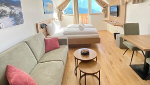 Ein Zimmer mit Bett, Sofa, kleinem Tisch, Fernseher und Fenster mit Bergblick.