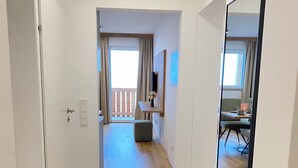 Ein Flur, der zu einem Balkon mit Holzboden, einem Essbereich mit Tisch und Stühlen sowie einer grünen, gepolsterten Bank führt.
