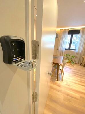 A room with a built-in charging station on the door, a dining area with a table and chairs, and a window with curtains. - STAYMADRID - Chic Apartment (MADRID)