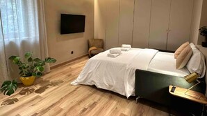 Ein modernes Hotelzimmer mit einem Bett, einem Sessel, einem Schreibtisch, einem Flachbildfernseher und einer Topfpflanze.