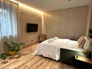 Ein modernes Hotelzimmer mit einem Bett, einem Sessel, einem Schreibtisch, einem Flachbildfernseher und einer Topfpflanze.