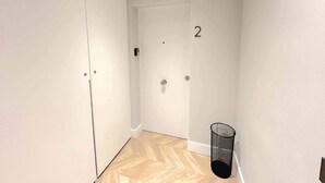 Ein Flur mit einer Tür, die die Nummer 2 trägt, einem Mülleimer und einem Holzboden.