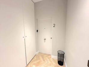 Ein Flur mit einer Tür, die die Nummer 2 trägt, einem Mülleimer und einem Holzboden.