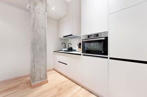 Eine moderne Küche mit weißen Schränken, einer schwarzen Arbeitsplatte und Edelstahlgeräten, darunter ein Backofen und eine Dunstabzugshaube.