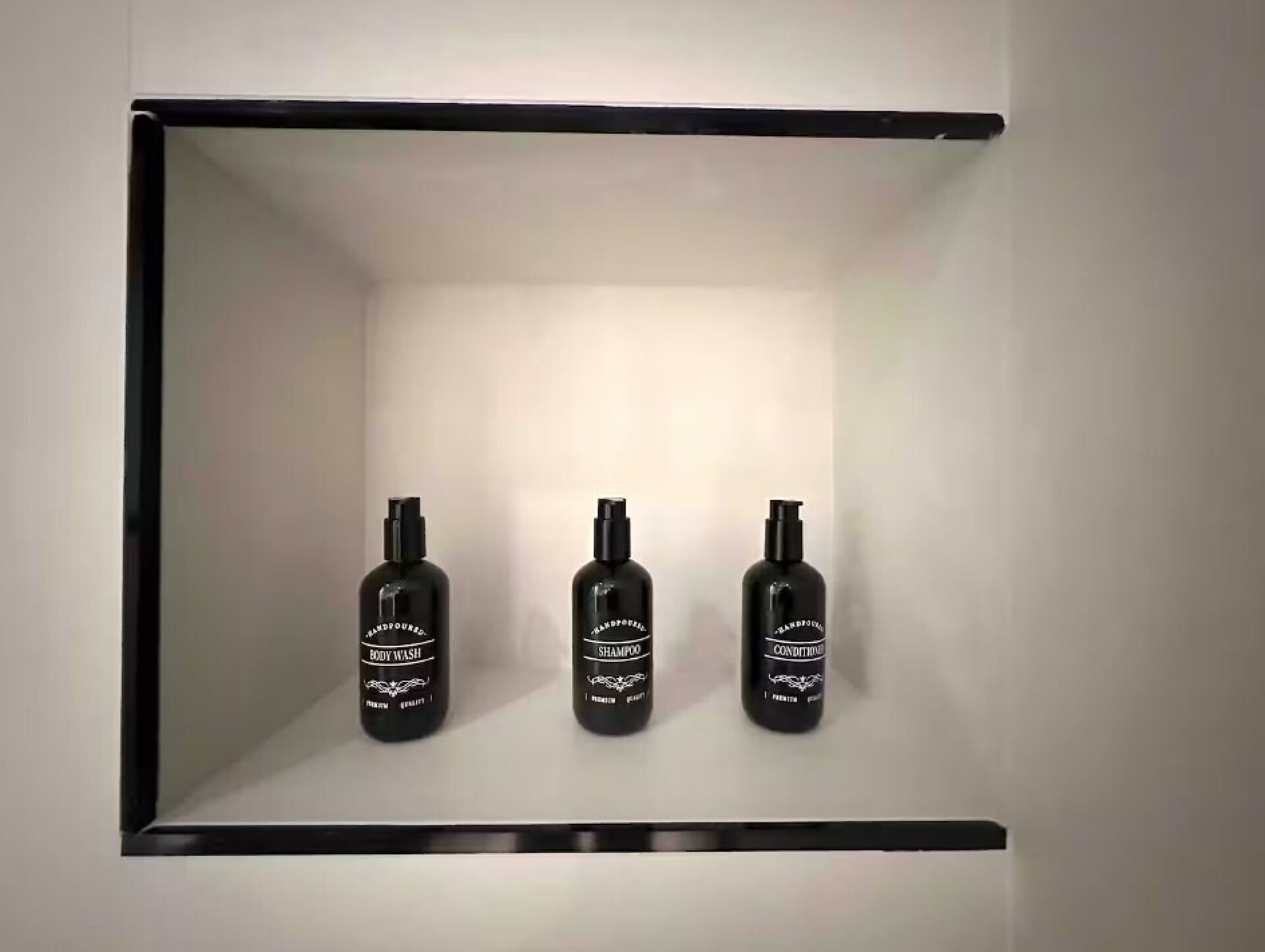 Une étagère avec trois bouteilles de gel douche, de shampoing et d’après-shampoing.