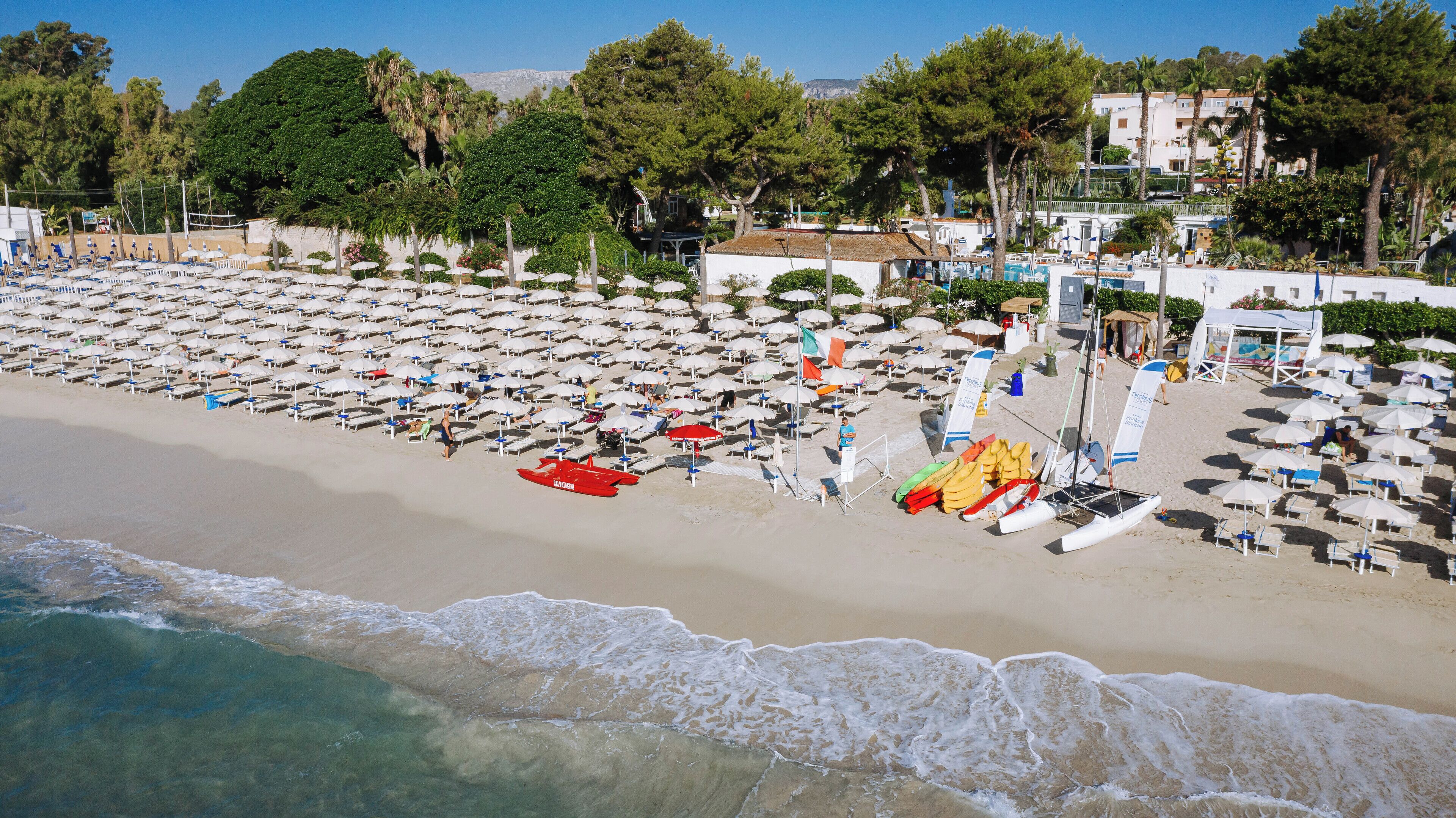 A beach with rows of umbrellas and sun loungers, a lifeguard tower, and a sailboat.