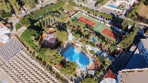 Vista aérea de un resort con múltiples canchas de tenis, una piscina y una amplia zona cubierta con sombrillas.