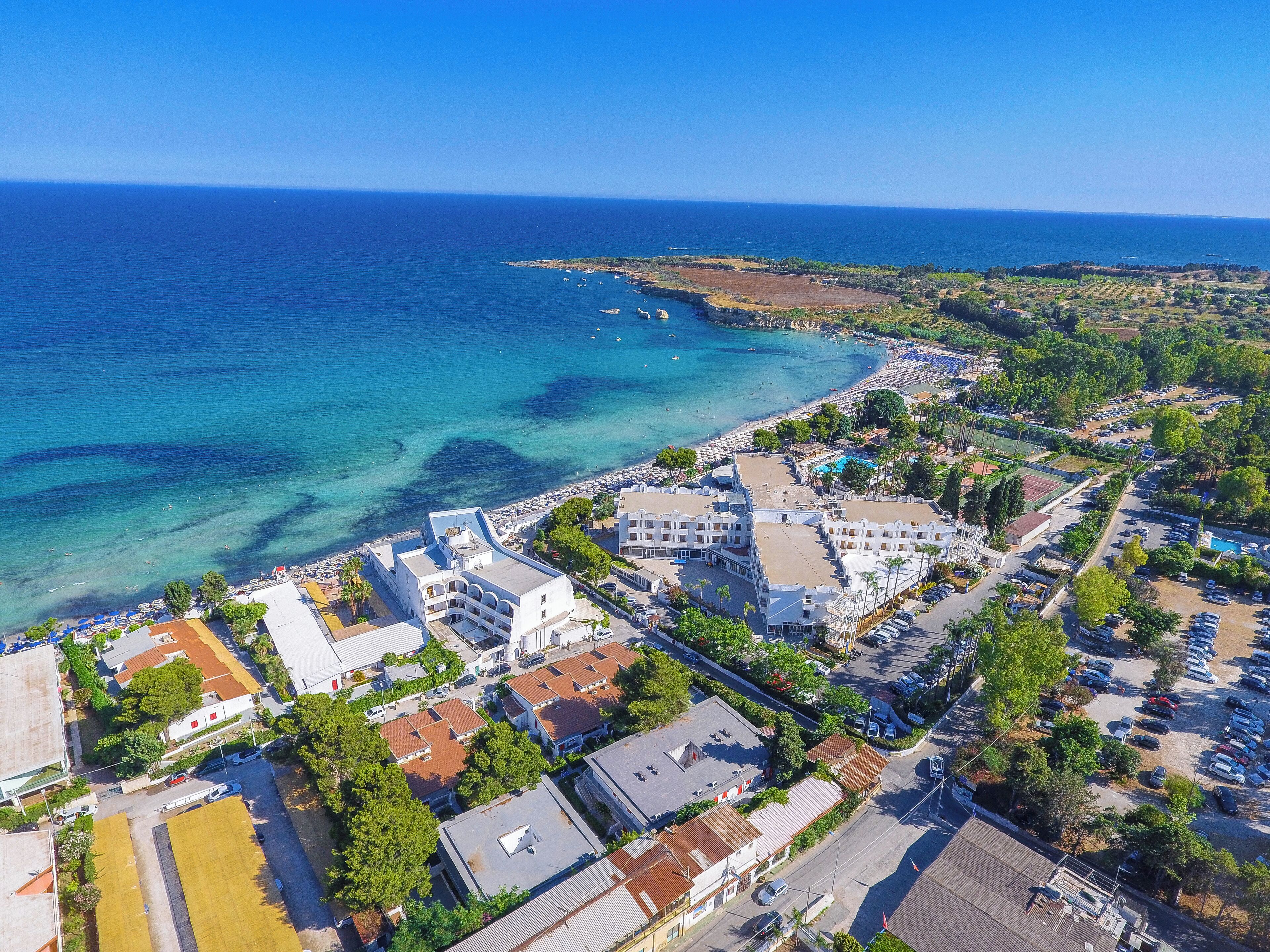 An aerial view of a coastal town with buildings, a beach, and clear blue waters.