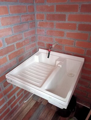 Een wit wastafel met een rode kraan tegen een bakstenen muur.