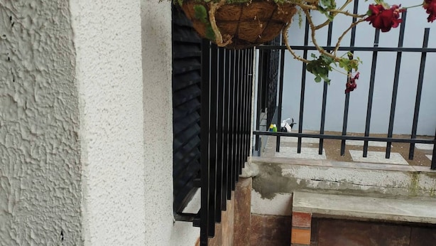 Un patio con suelo de piedra, pared blanca y valla de metal negro.
