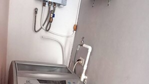 Una lavadora compacta y moderna con un panel de control digital, ubicada en un rincón de una habitación con pared gris.