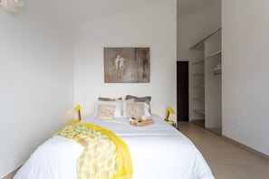 A neatly arranged bedroom with a bed, bedside lamps, a bedside table, a wall-mounted artwork, and a closet.