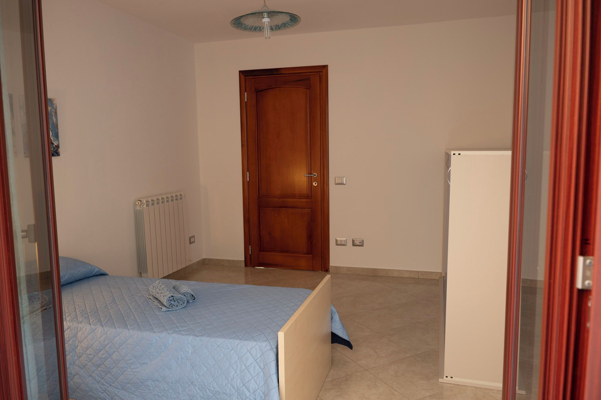 Une chambre à coucher avec un lit, une porte en bois, un radiateur et une armoire blanche.