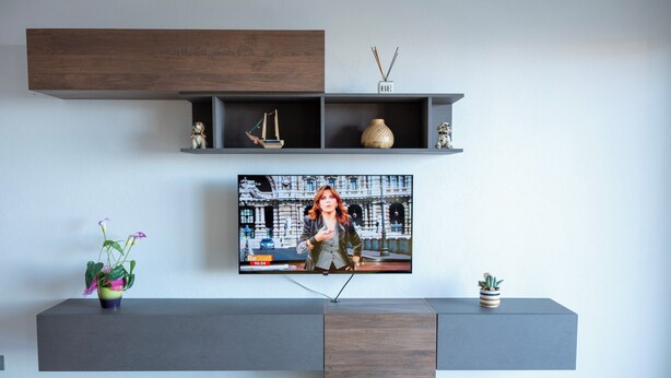 A modern living room with a flat-screen TV mounted on a wall, a grey console table below, and decorative items including a small ship model and a vase. - House Gennauara (Lanusei)