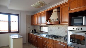 A kitchen with wooden cabinets, a built-in oven, a microwave, and a gas stove. - House Gennauara (Lanusei)