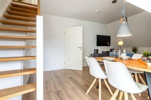 Une cuisine moderne avec un plancher en bois, des armoires blanches et un coin repas comprenant une table en bois et des chaises blanches.