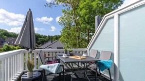 Un balcon avec une table et des chaises, un pot de fleurs et un parasol.