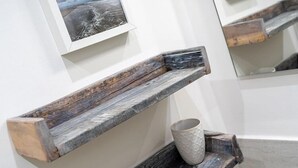 Une étagère en bois rustique, sur laquelle repose une tasse, est fixée à un mur blanc, au-dessus de laquelle on peut voir un tableau encadré.