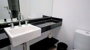 Een moderne badkamer met een witte wastafel, een zwart aanrechtblad en een wit toilet.