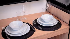 Een net gedekte eettafel met witte borden, zwarte placemats en glanzende wijnglazen.