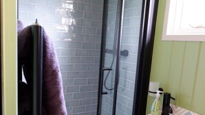 A bathroom with a glass-enclosed shower, a white sink, and a window. - Shepherds Hideaway (Holsworthy)