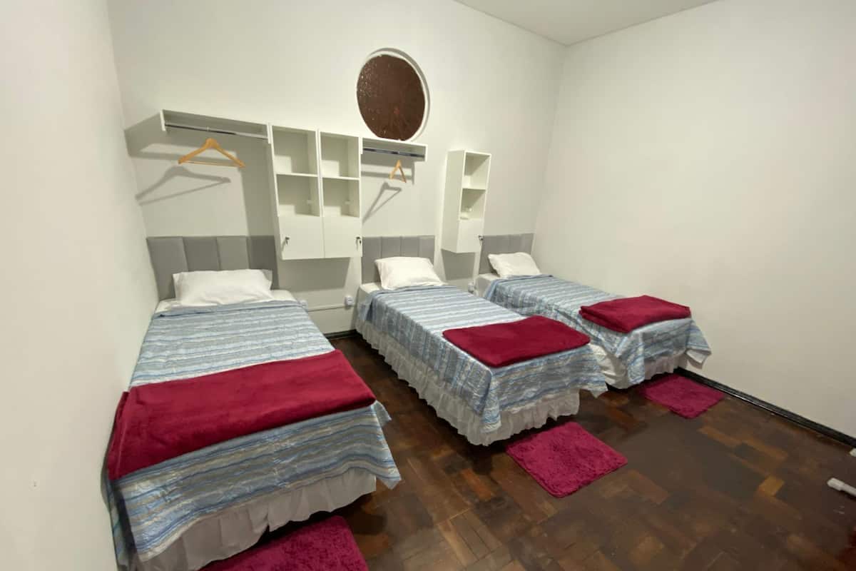 Une chambre avec trois lits, une armoire, un miroir et une petite fenêtre ronde.
