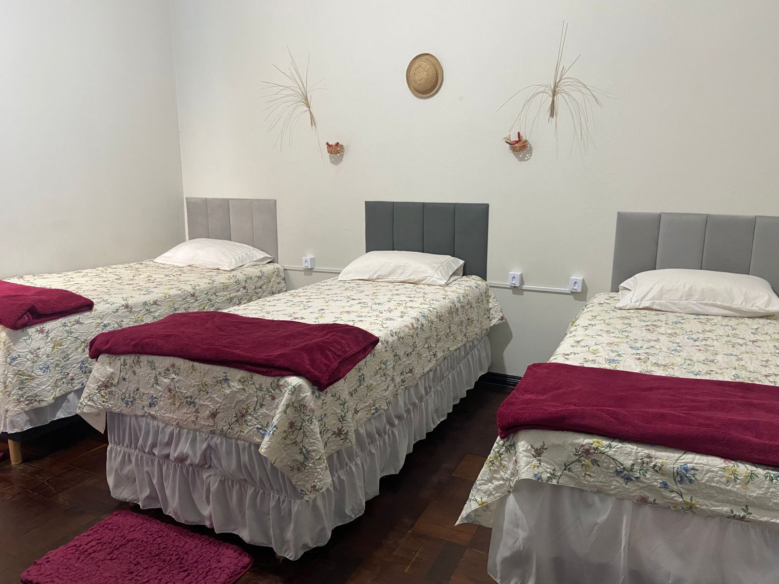 A hotel room with three single beds, each with a floral bedspread and a red throw blanket.